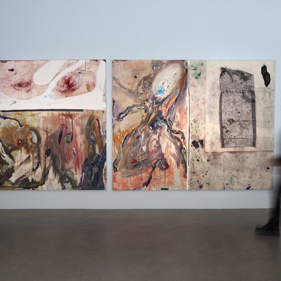A person walks past two paintings by Manuel Mathieu, hanging on a light blue wall.