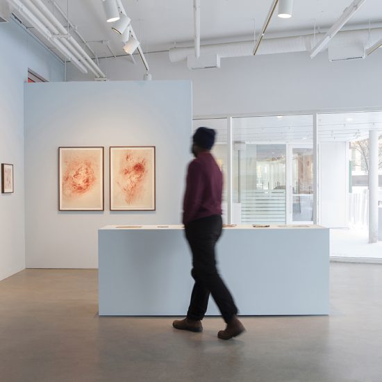 A person walks past a three foot high plinth towards the corner of gallery 1, where drawings are hung.