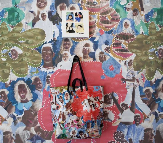 Close-up view of the tote bag hanging on the gallery wall. The tote and the wall are decorated with the same collage pattern. Above, a tee shirt with 4 loosely painted faces is stretched onto a canvas.