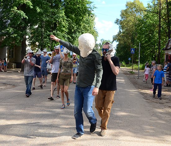 A parade is happening, the person leading is wearing a white mask while waving