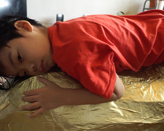 A child wearing a red shirt laying down on gold shimmery object
