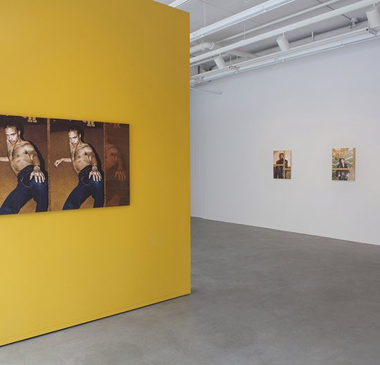 View of large yellow wall in which a diptych hangs. Across from it 3 small photographs hang on a separate wall