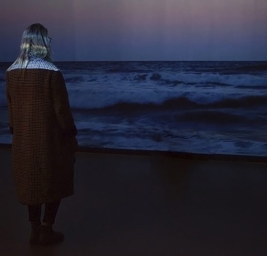 Woman stands in front of projection of ocean