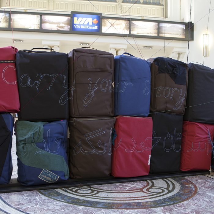 Several soft sculptures that resemble luggage are stacked together. The words "Carry your Story" are embroidered across them.