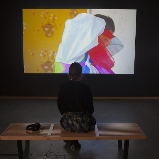 A woman sits on a bench in front of a video projection