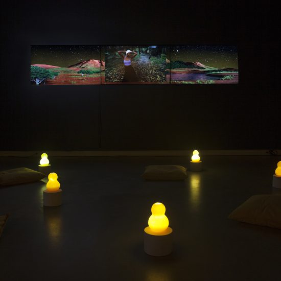 A dark room, 3 tv's play video's along the right wall. Illuminated calabashes are scattered on the floor