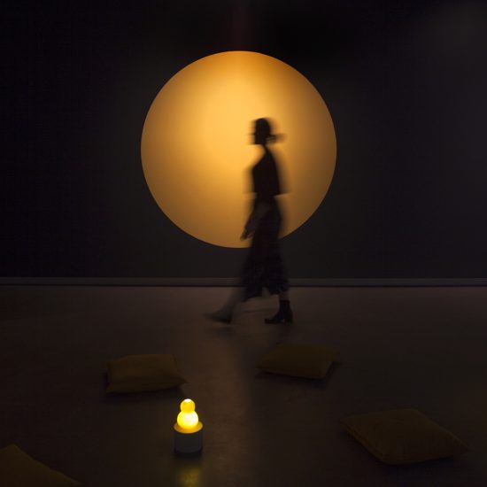 Large yellow circle painted on a black wall, a blurred figure stands mid step in front of it