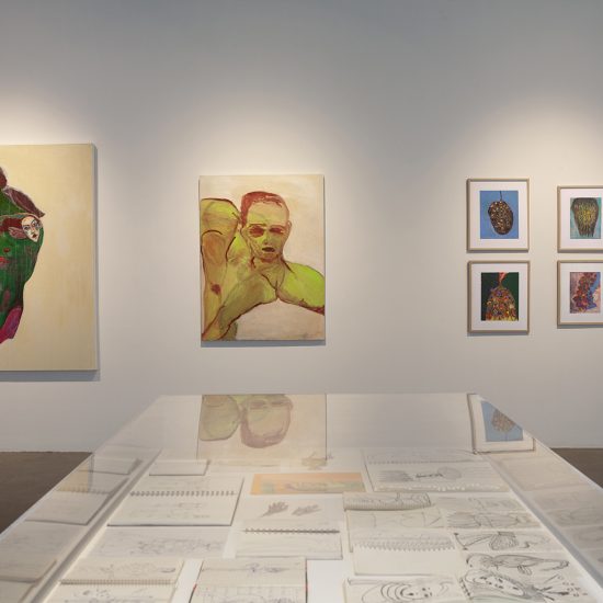 Interior gallery 2, large paintings hang on a white wall, a glass top vitrine is in the foreground