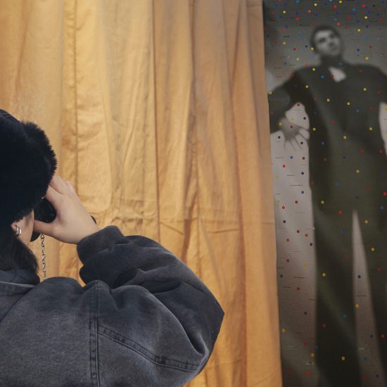 A woman looks through binoculars next to a brown curtain. A print of a man hangs in the background