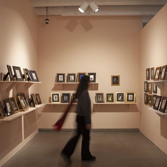 The gallery walls are painted a light pink, each holds 2 shelves with multiple small picture frames on them