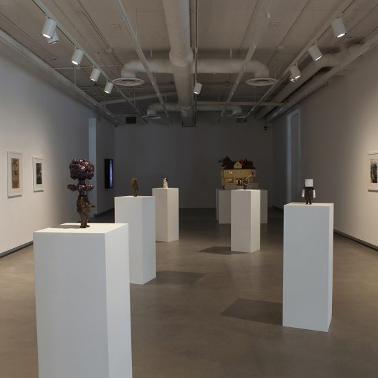 Point of view from entrance of gallery 1. Six white rectangle podiums, five of which showcase smaller mixed media statues, the last at the back has House on Fire. Pictures hang on both flanking walls.