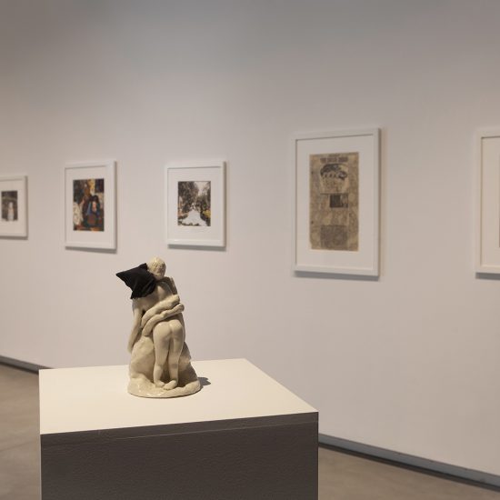 Rectangular white podium showcasing white figure statue in the foreground. Pictures hang in line on wall behind.